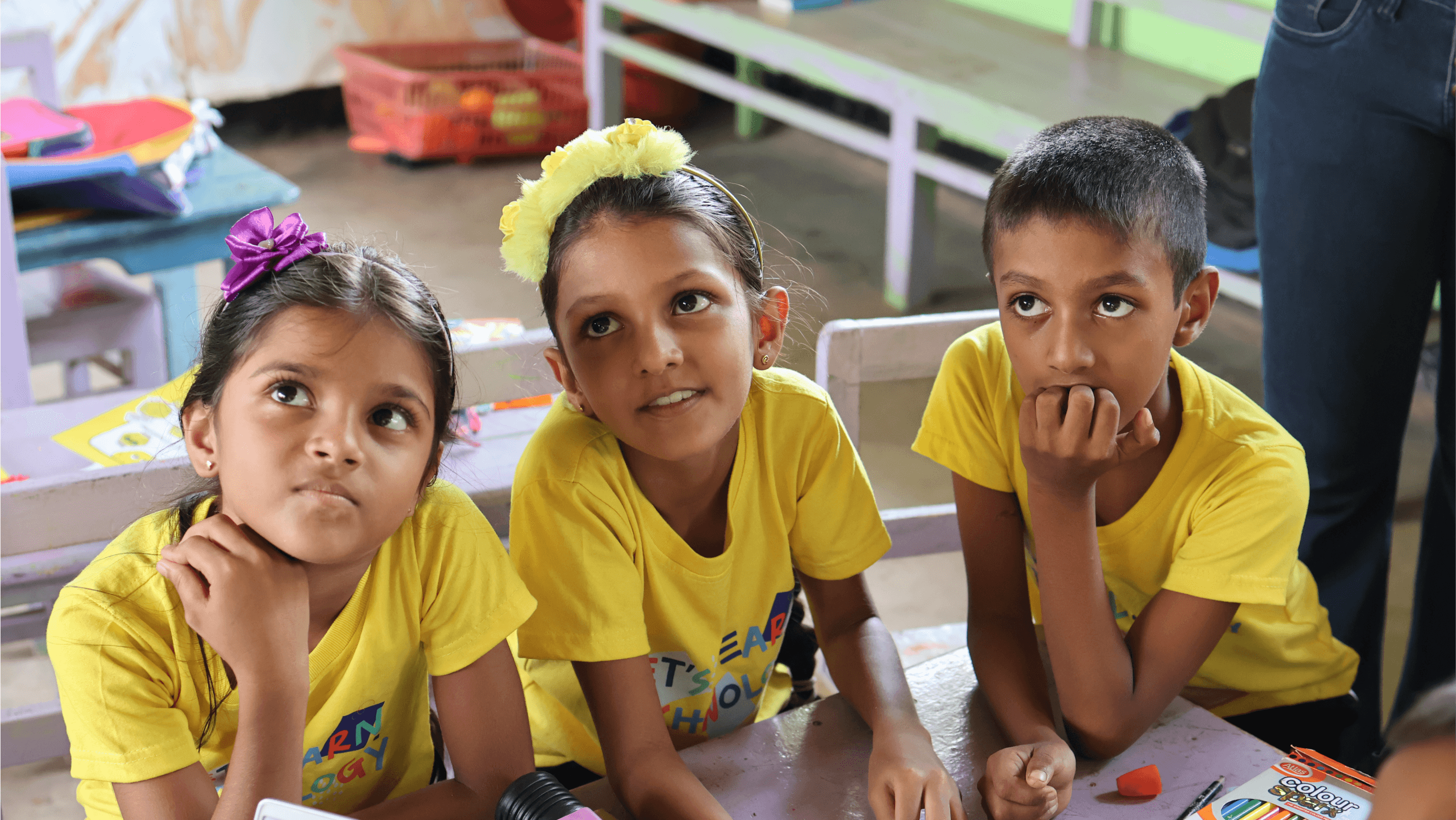 Children in yellow shirts looking attentive in a classroom